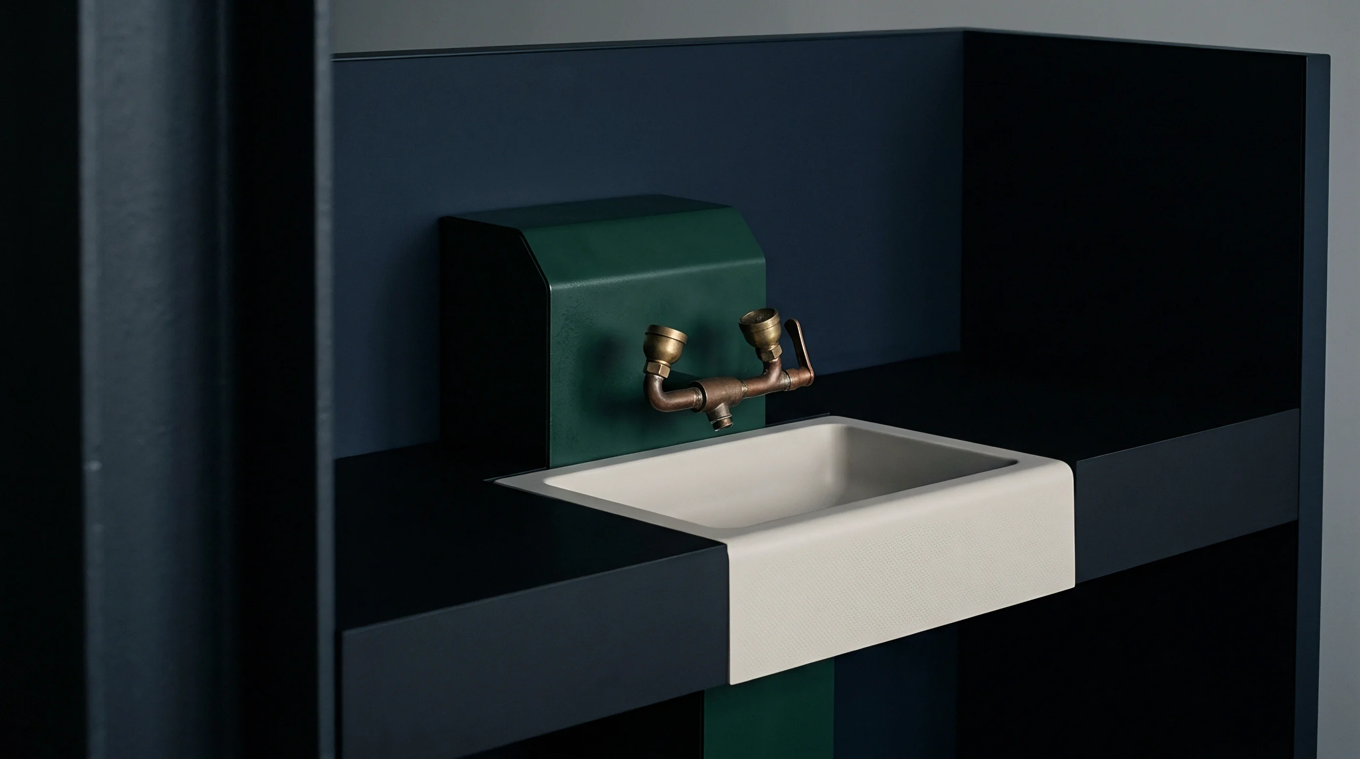 A matte white ceramic basin features brass plumbing and a green metal enclosure integrated into a dark industrial workstation wall.